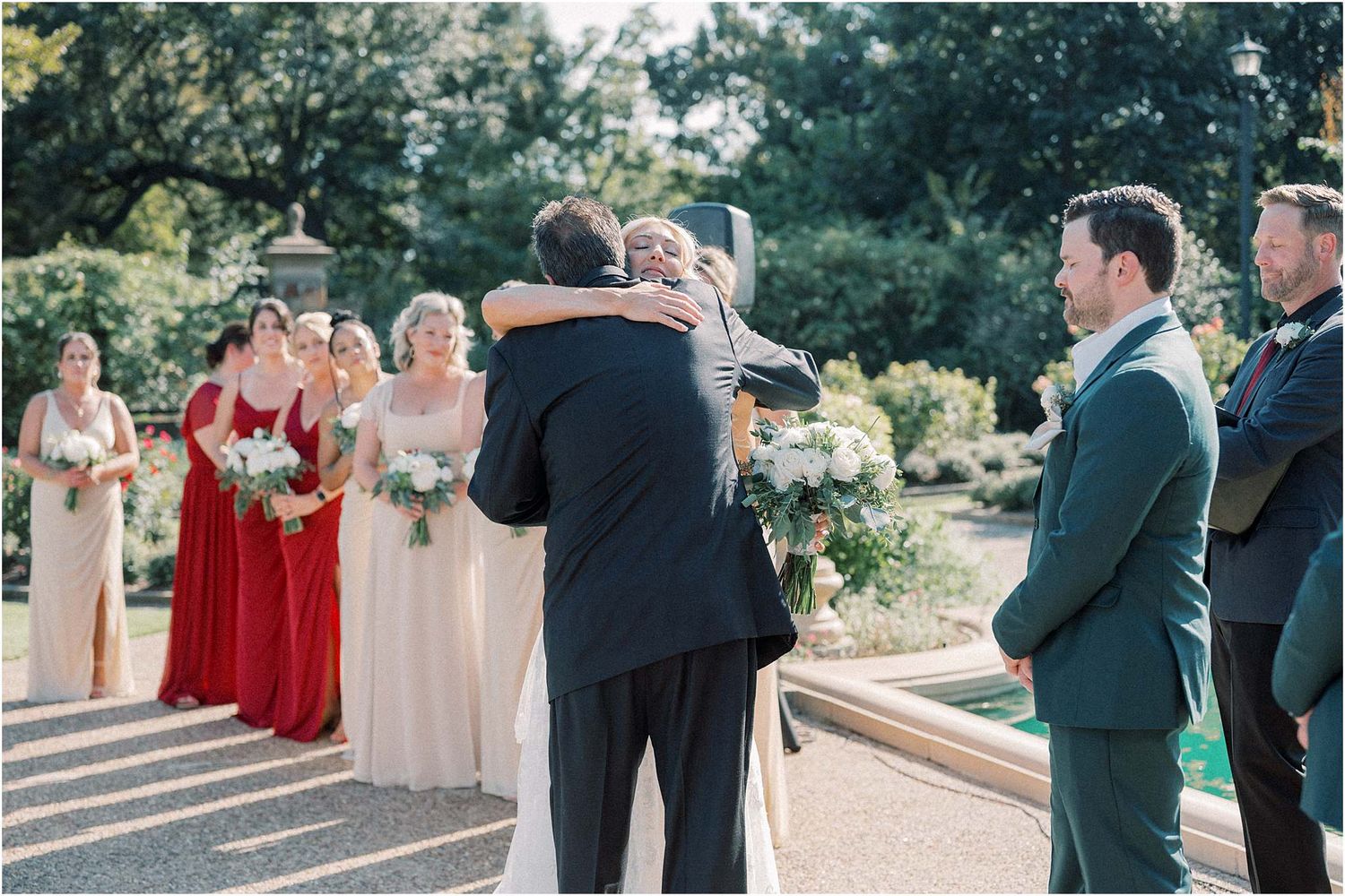 Wedding party in red and neutral dresses gathered outdoors for ceremony photos.