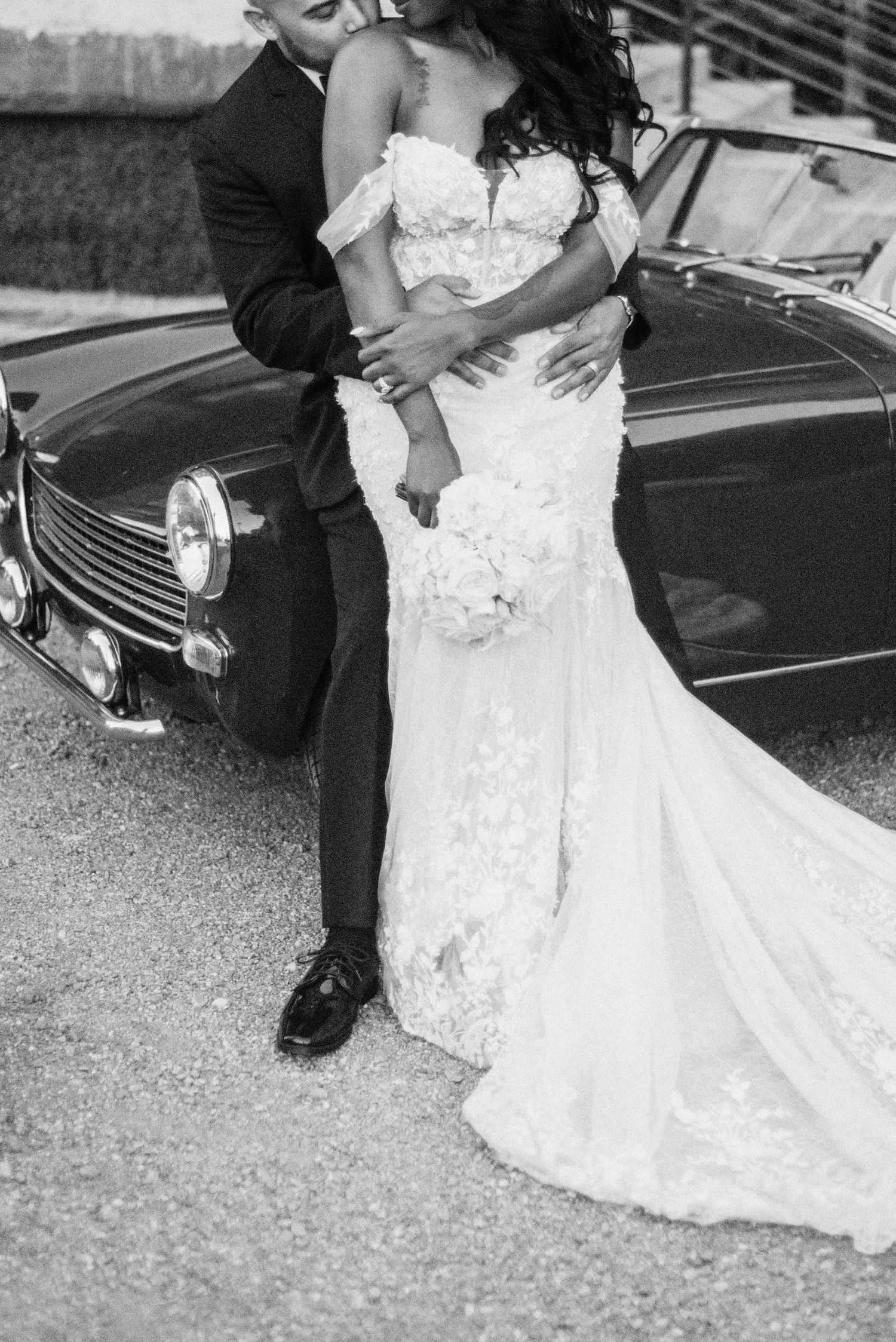 Wedding couple poses by vintage car showing details of lace wedding dress.