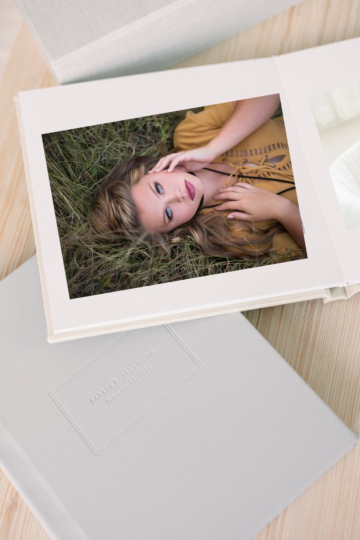 A young woman with long hair lies in green grass, wearing a golden dress, featured on a white photo album cover.