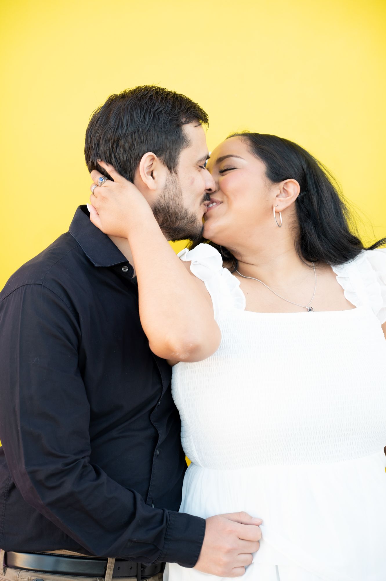 A couple in black and white outfits share a romantic kiss against a bright yellow background.