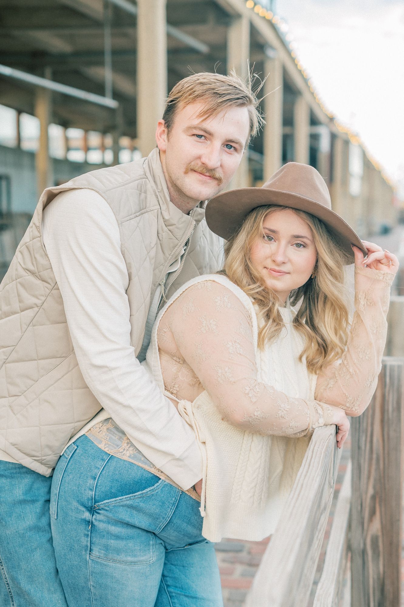 A couple in coordinated outfits posing playfully against a rustic building backdrop.