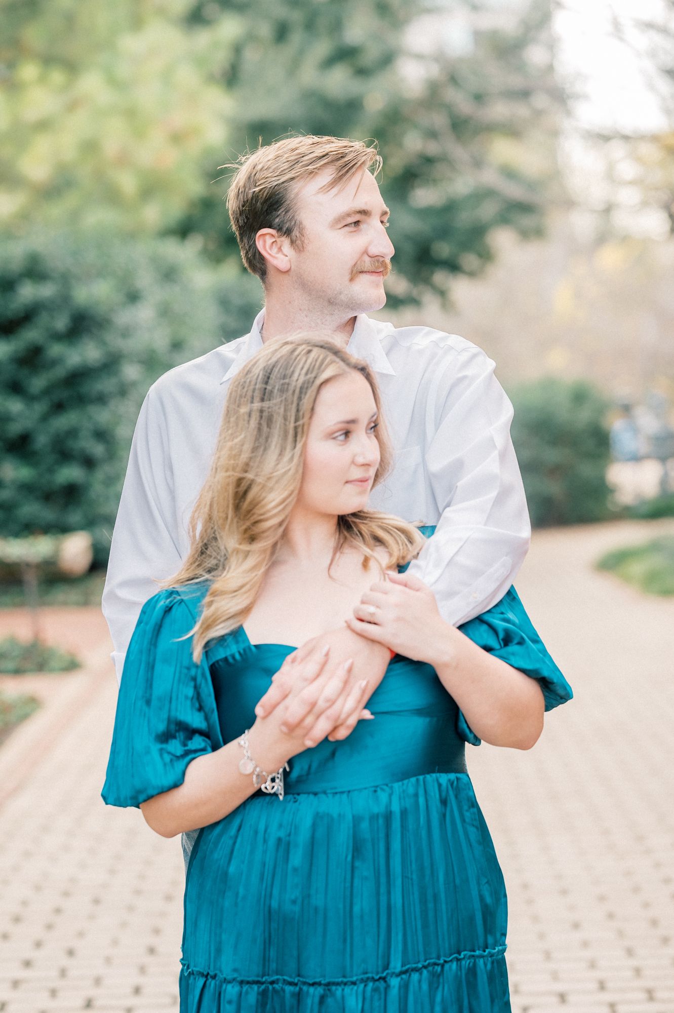 A romantic couple embraces outdoors in coordinating teal and white outfits during a sunny photo session.