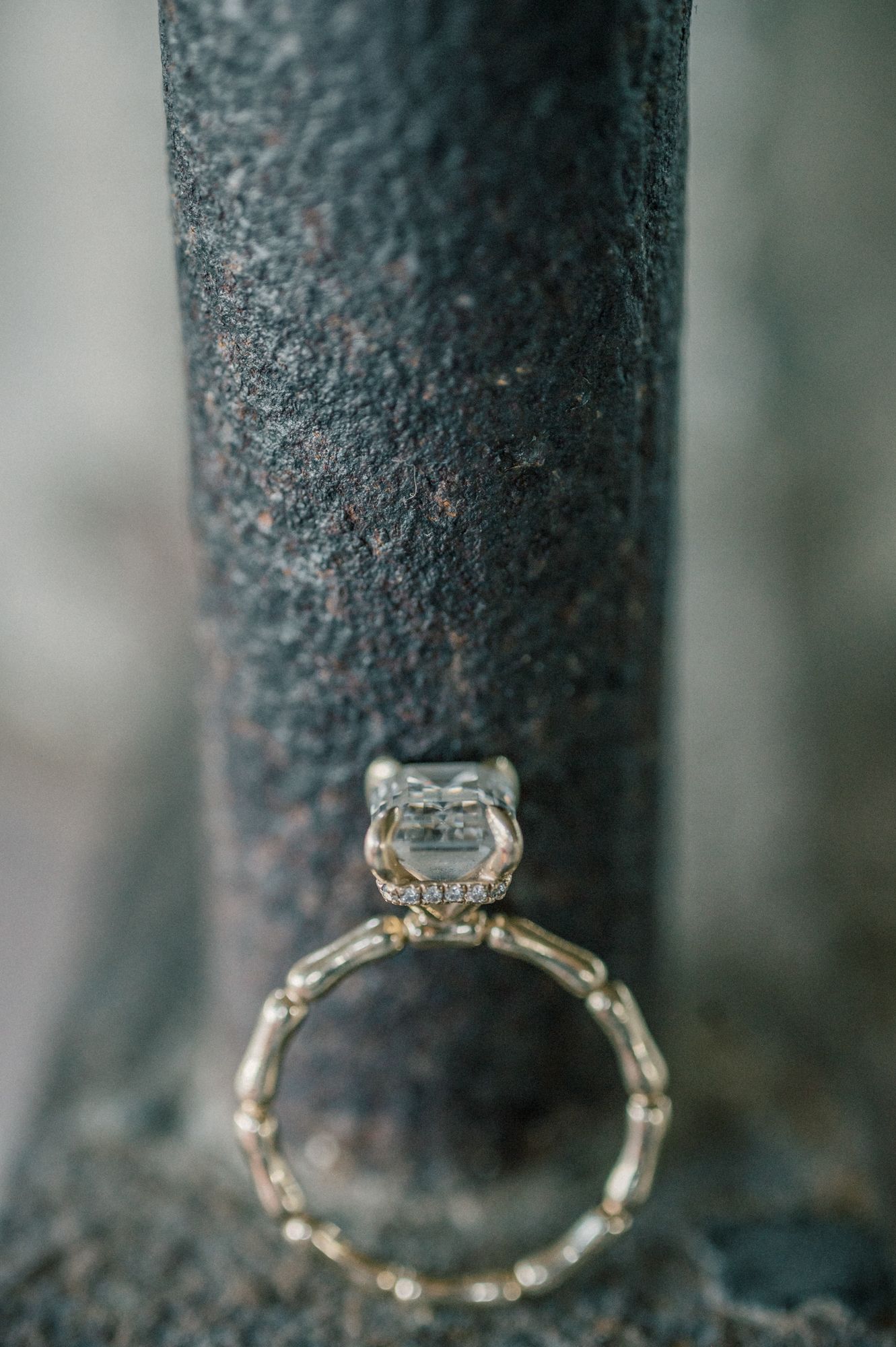 Close-up detail shot of an elegant diamond engagement ring against a textured dark surface.