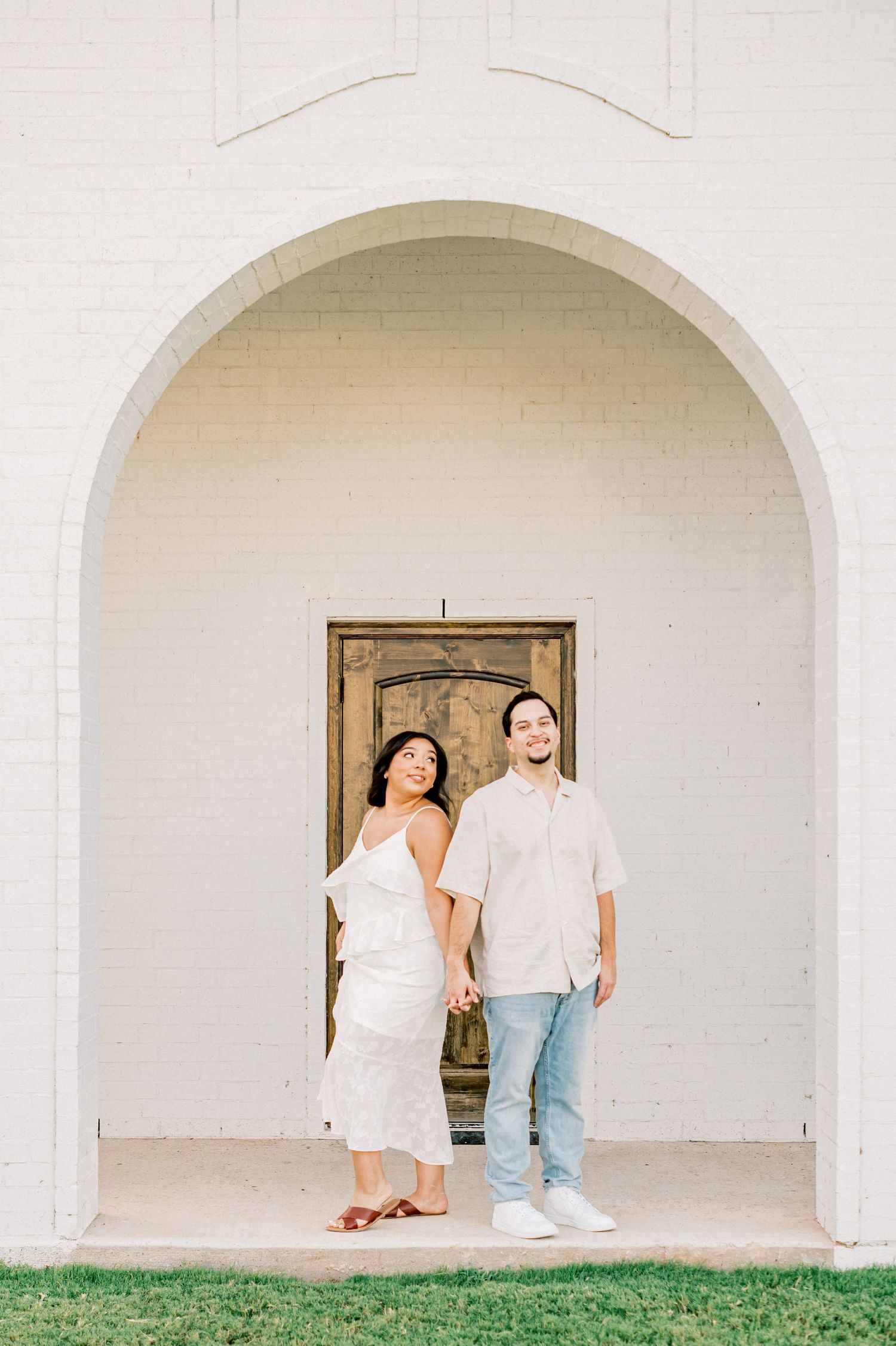 A couple poses together under white arched walkways against a clean architectural backdrop.