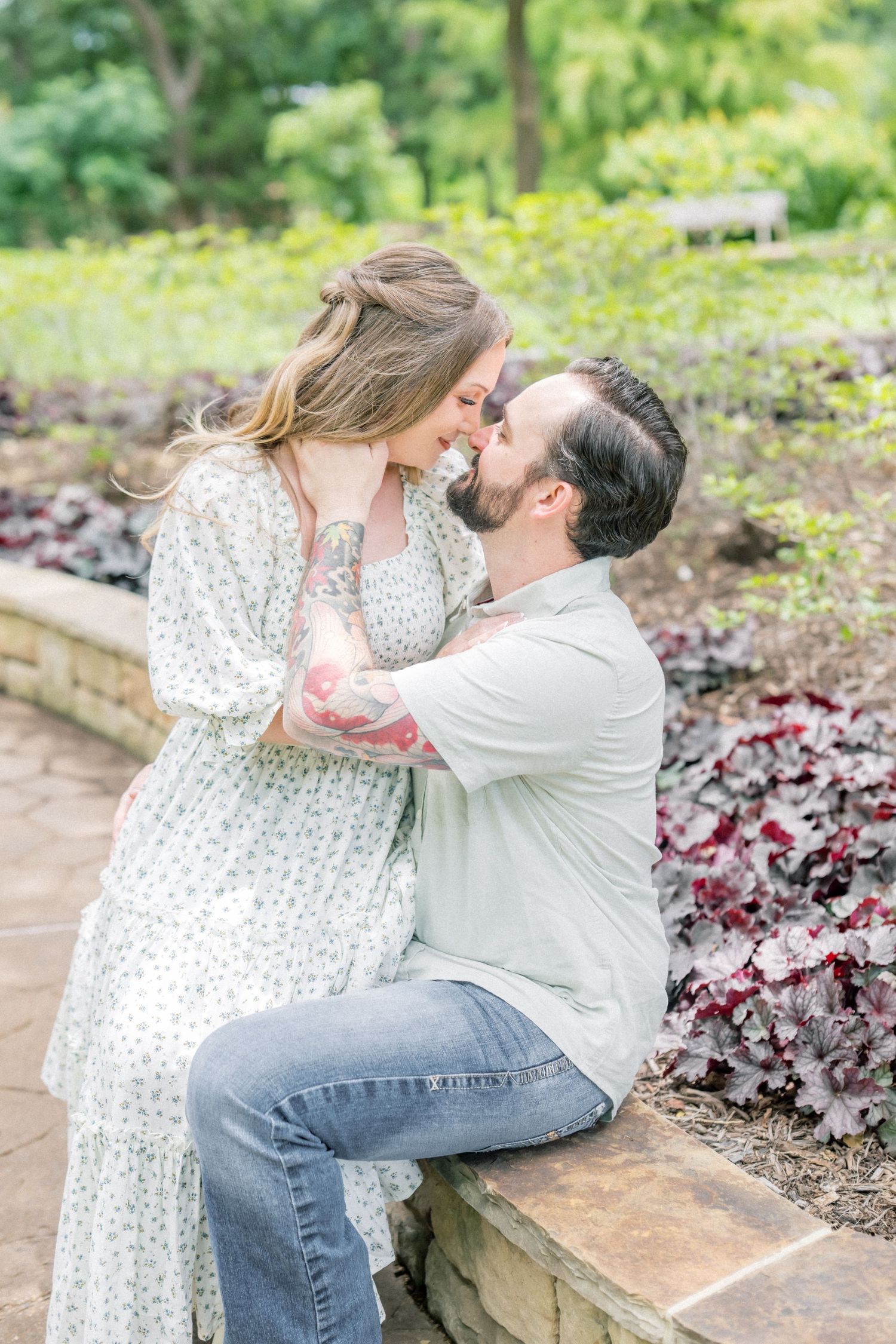 Couple sharing a romantic nose-to-nose moment seated by a garden stone wall.