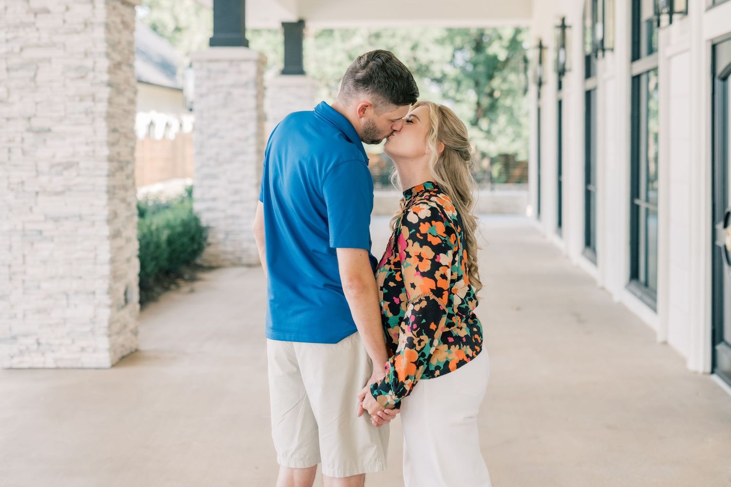 A couple leans in for a kiss while holding hands on a covered outdoor walkway.