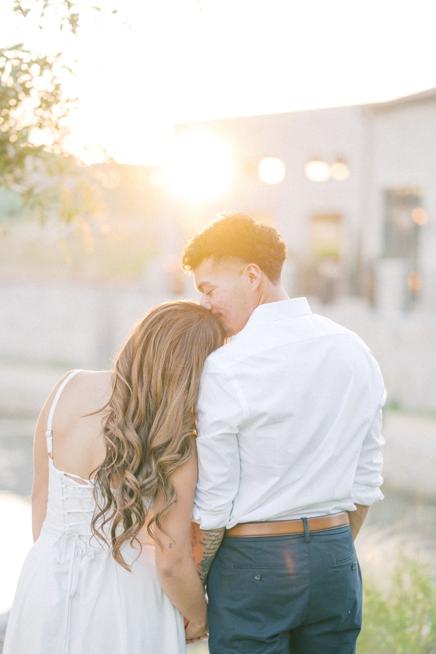 A couple shares a tender kiss bathed in warm golden sunset light during their romantic engagement session.