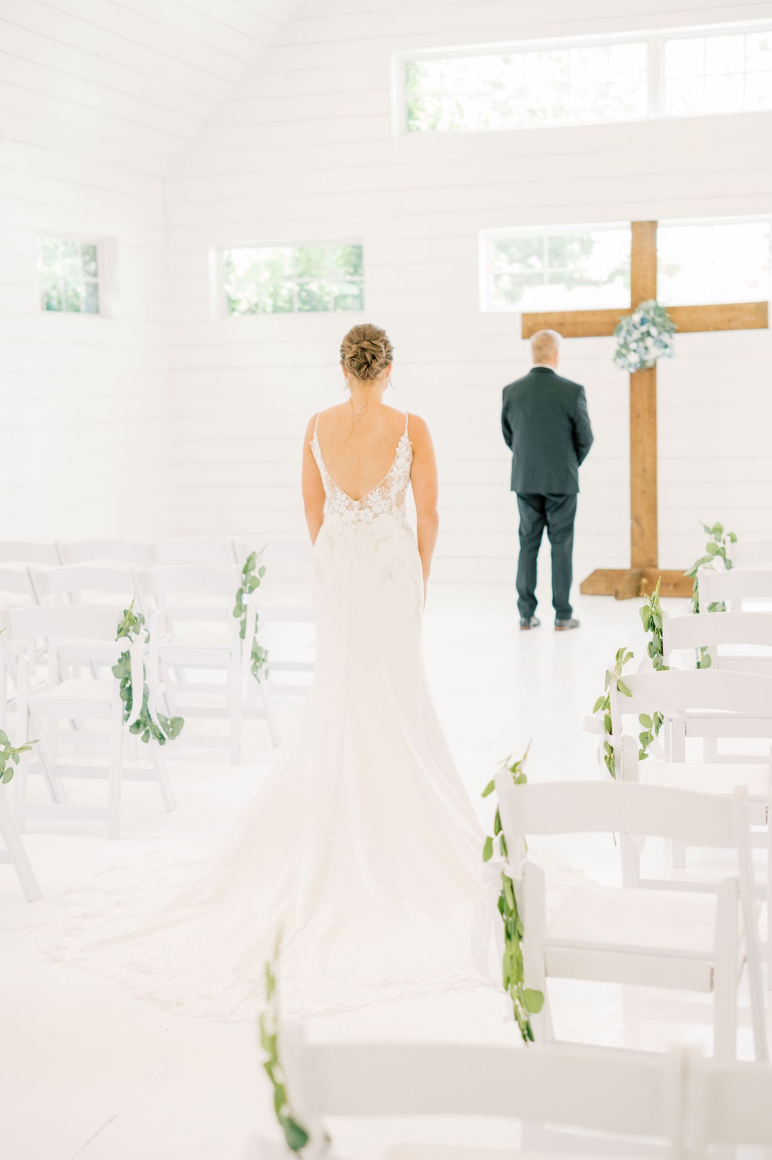 Light-filled chapel interior decorated with greenery and white chairs for a wedding ceremony.