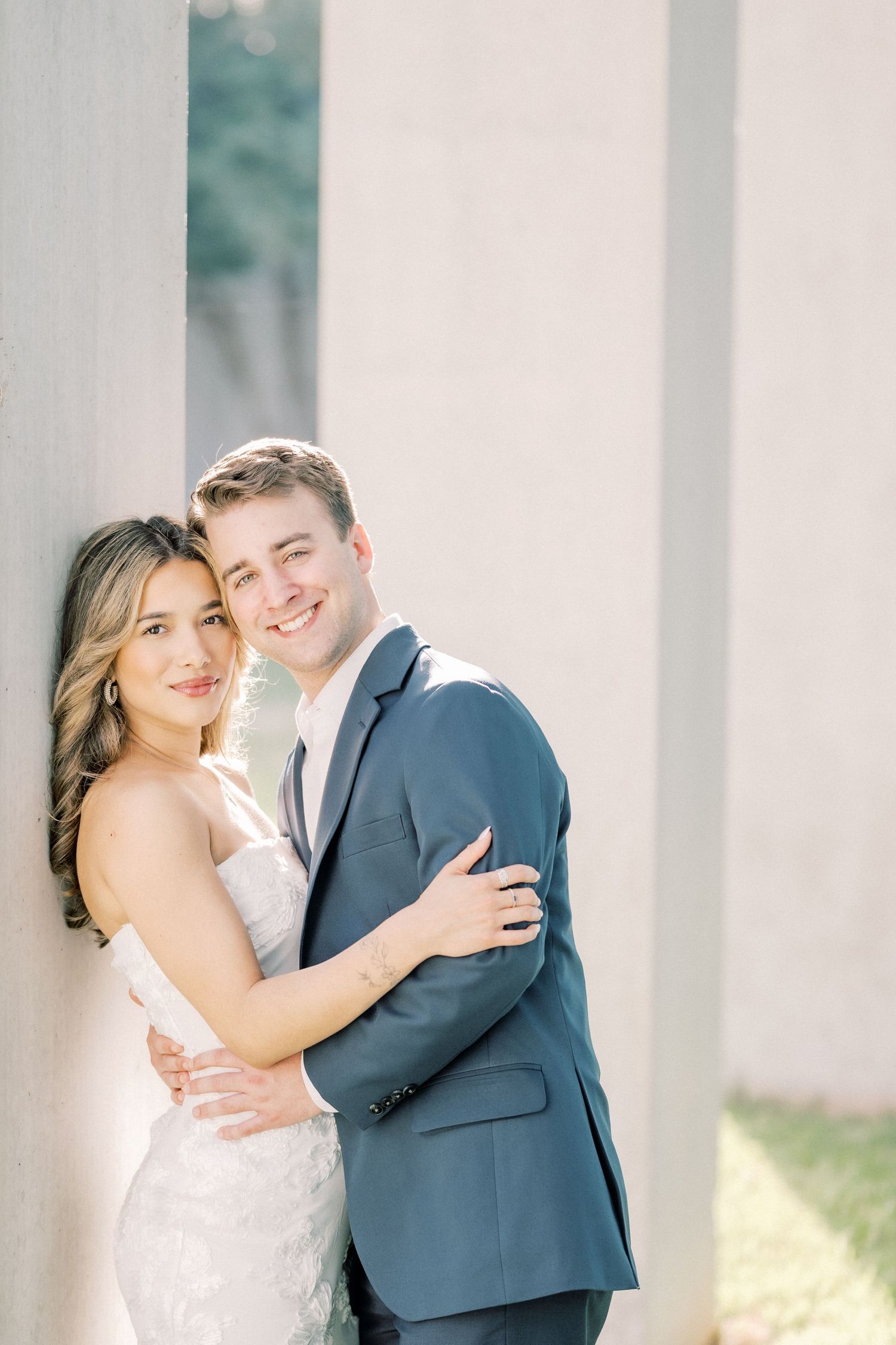A romantic wedding photo series showing a couple in formal attire embracing against white columns in soft lighting.