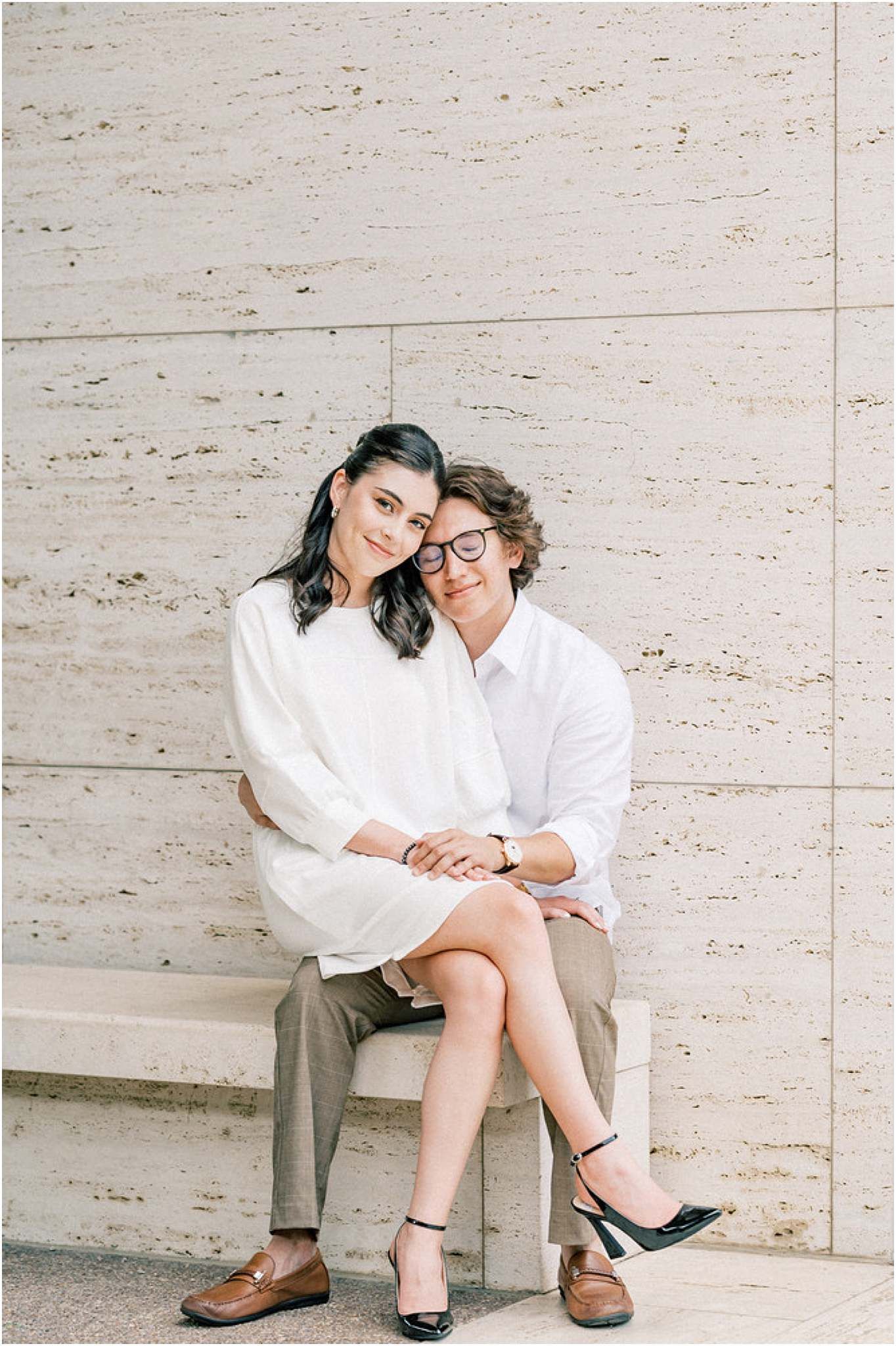 Couple in white shirts sitting together on stone bench showing affection and intimacy.