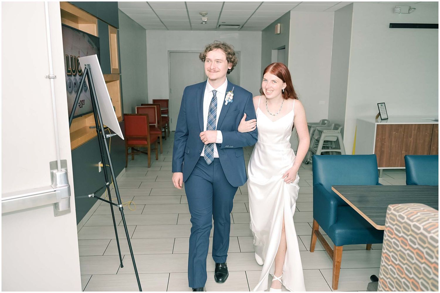 Wedding couple walking through bright indoor venue hallway.
