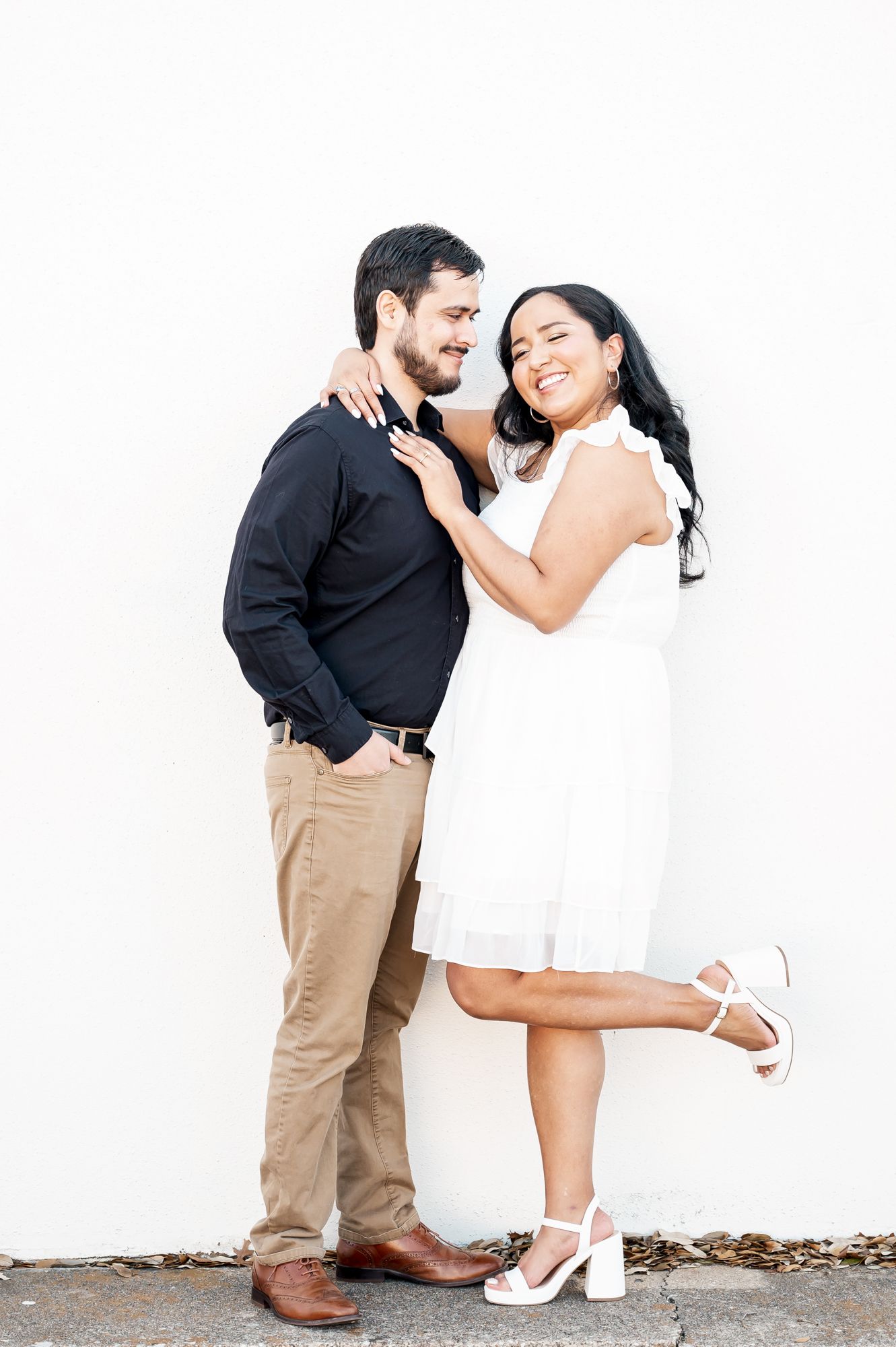 A couple in contrasting black and white outfits share romantic moments in a series of engagement photos against a wall.