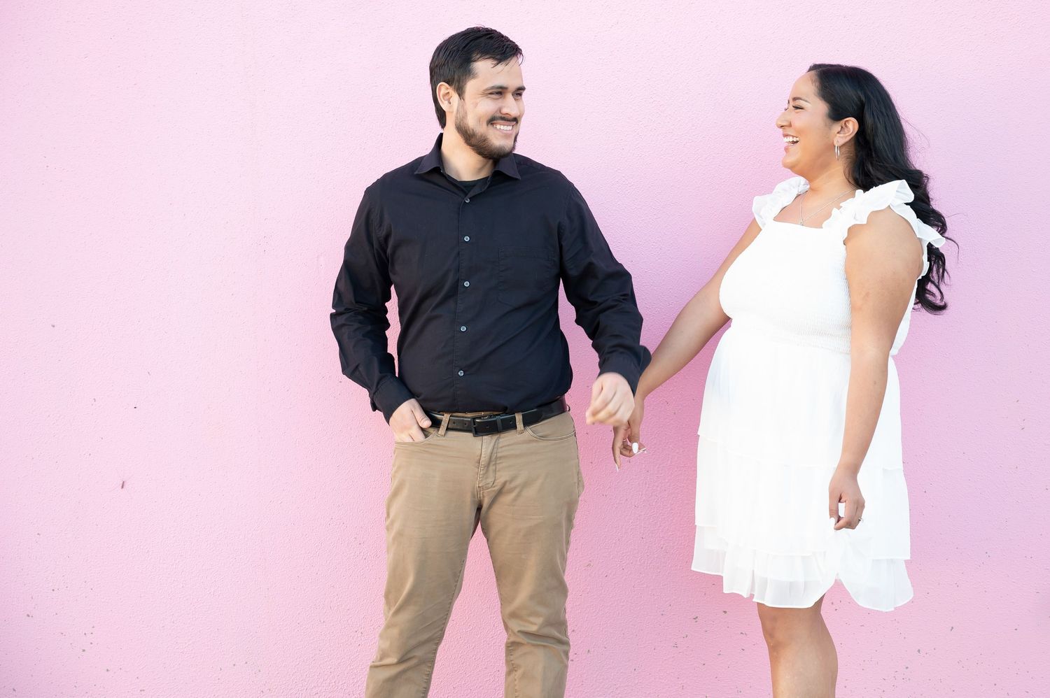 Two people dance and twirl together in front of a pink studio backdrop.