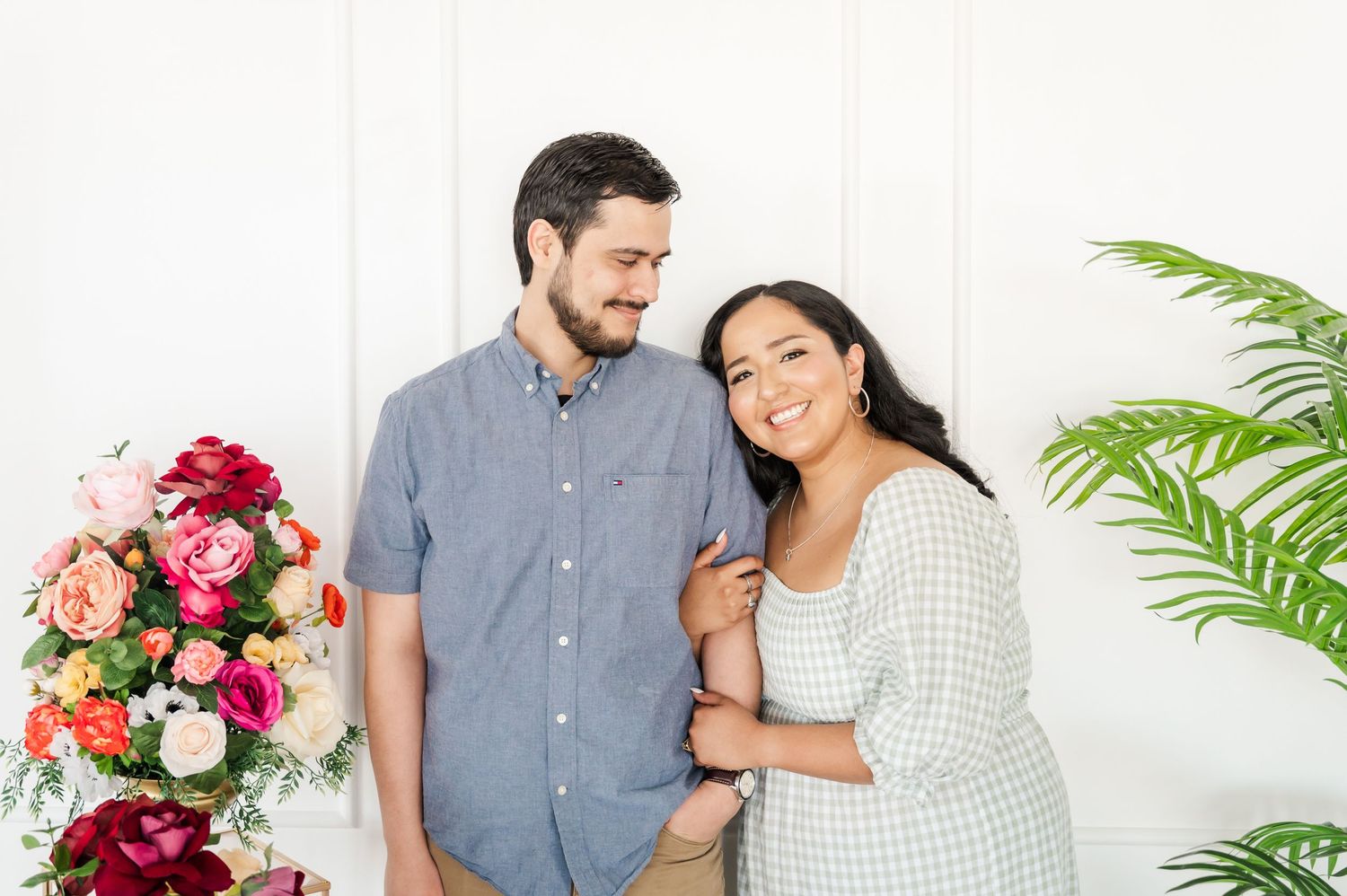 A sweet couple embraces near colorful floral arrangements and tropical plants.