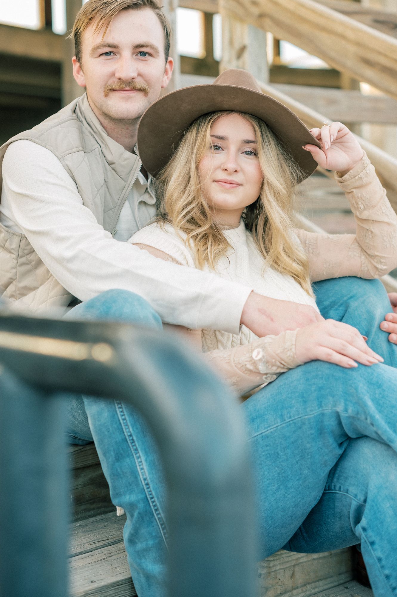Couple in western-inspired outfits posing intimately on wooden steps during photoshoot.