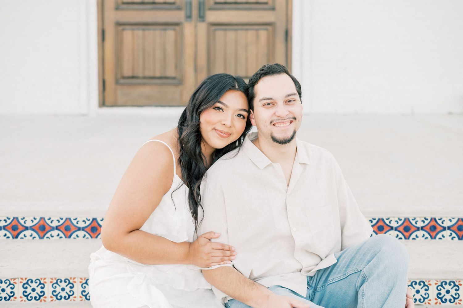 A couple sits close together on white steps decorated with traditional Mediterranean tile patterns.