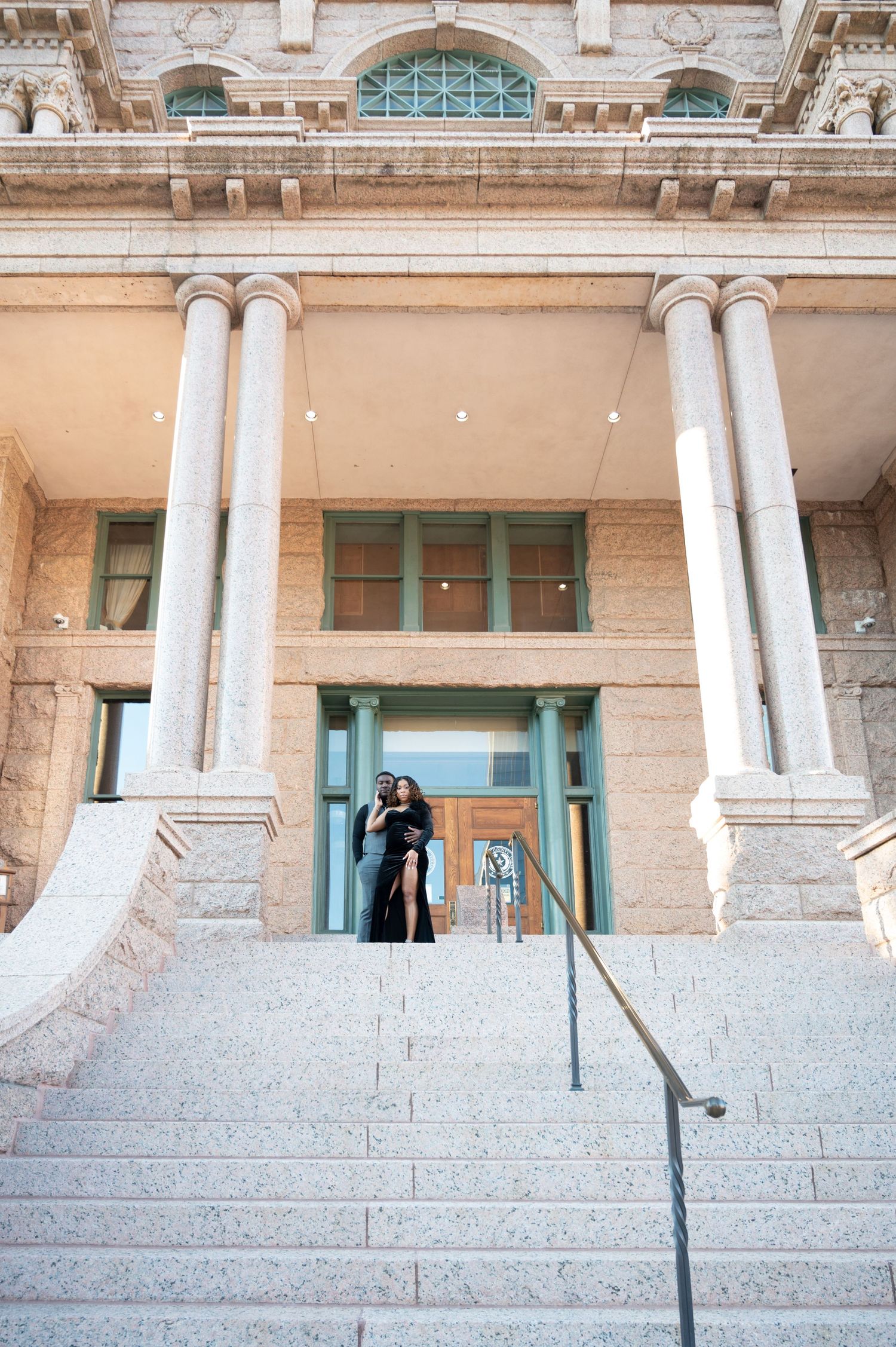 Couple posing on grand stone steps of a neoclassical building with tall columns during golden hour.