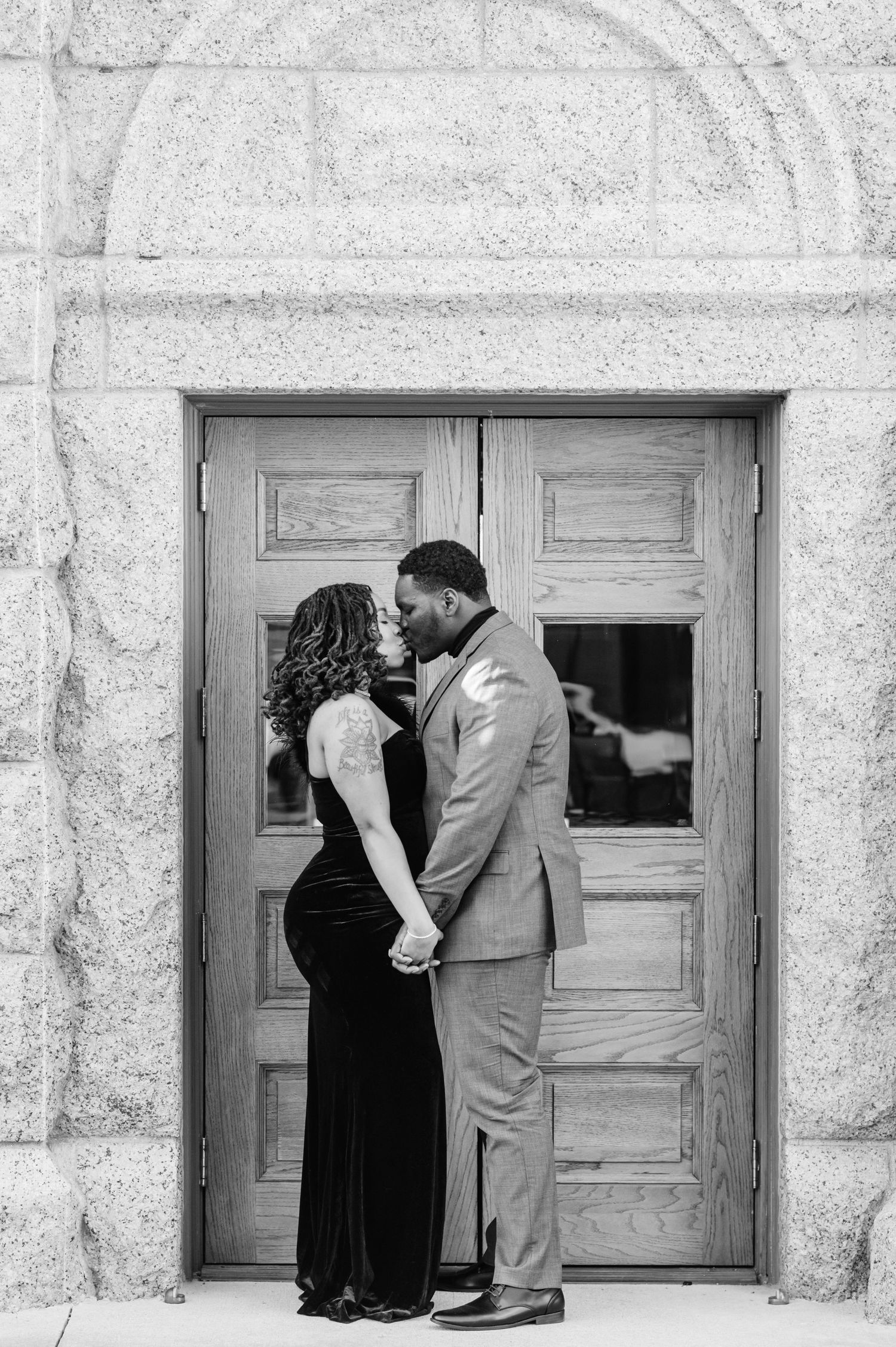 Black and white photo of a couple holding hands and kissing in front of elegant wooden doors.