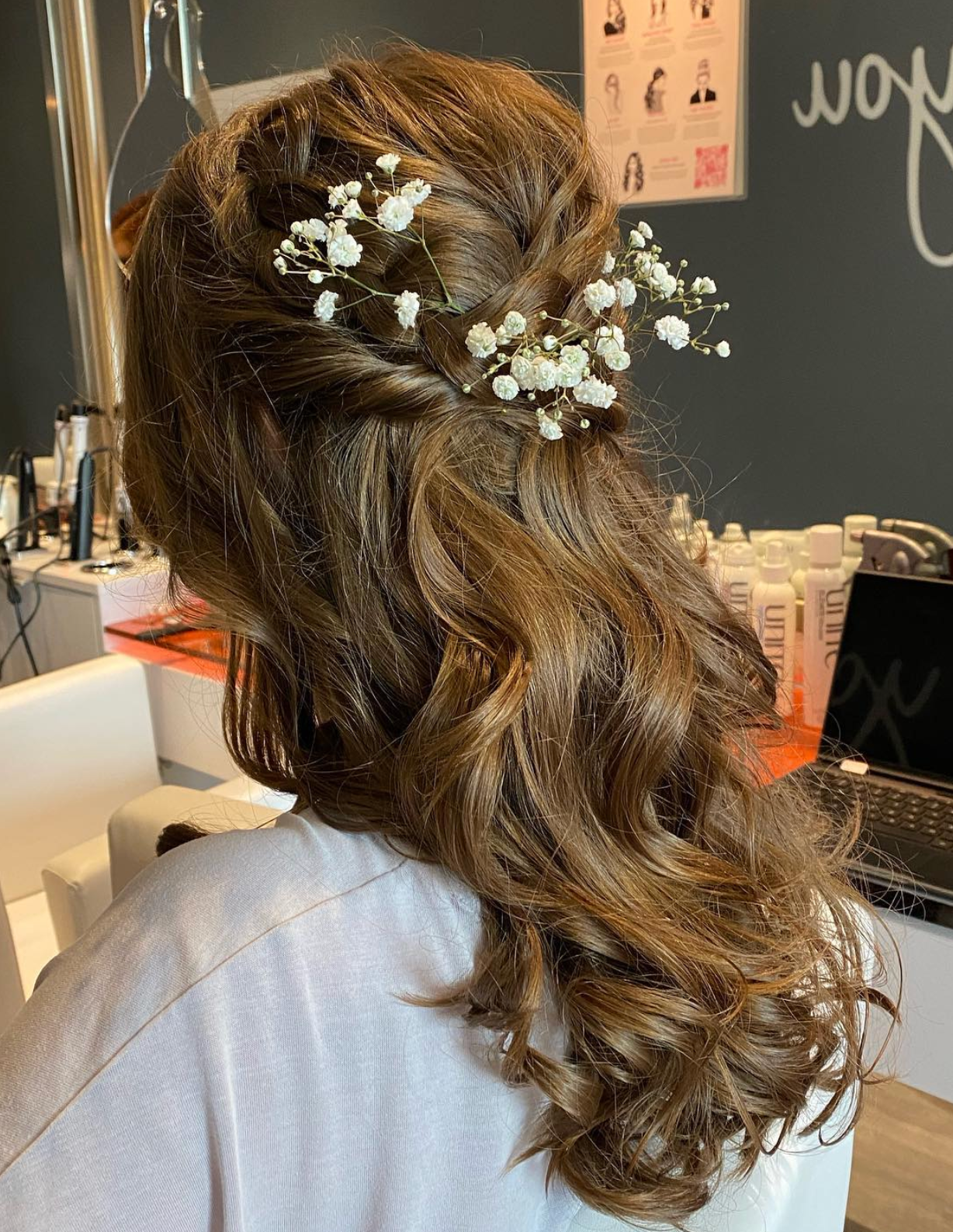 Elegant half-up bridal hairstyle with soft curls and delicate white baby's breath flowers on brown hair.