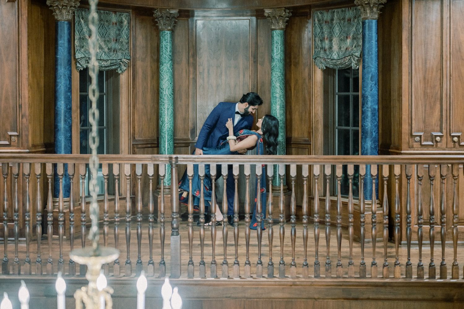 Romantic couple shares intimate moment on vintage wooden balcony with ornate details.