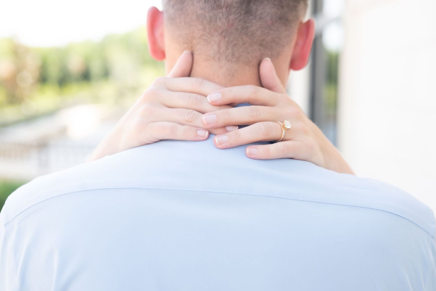 Person holding the back of their neck with both hands, suggesting neck pain or discomfort, outdoors background.