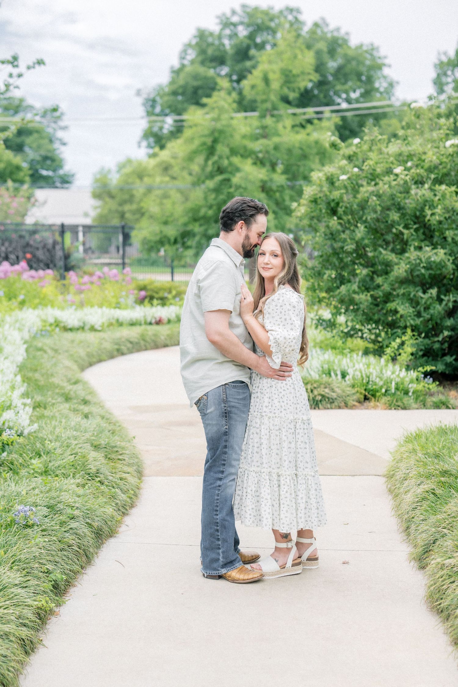 Couple embracing on a garden path surrounded by lush greenery and colorful flowers.