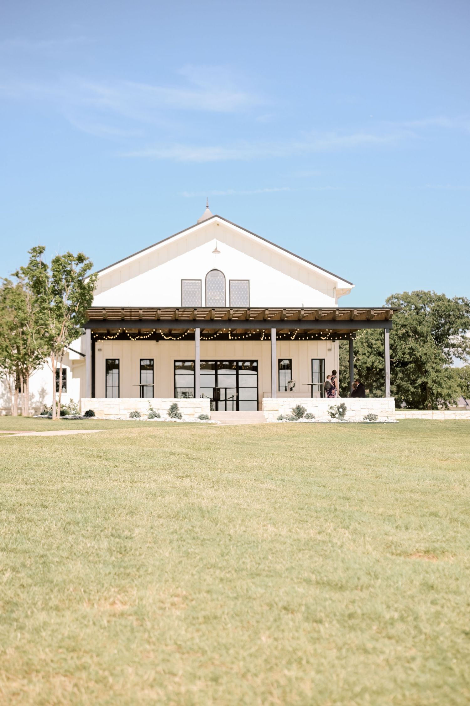 White barn wedding venue with large lawn under a clear blue sky surrounded by trees.
