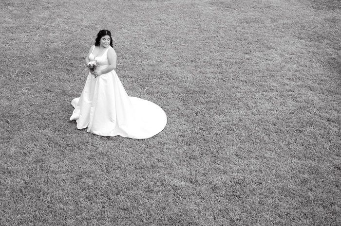 Black and white aerial view of bride in white gown with train standing on green lawn.