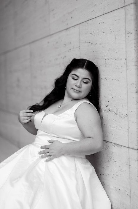 Black and white photo of a bride in a white gown leaning against a stone wall, eyes closed.