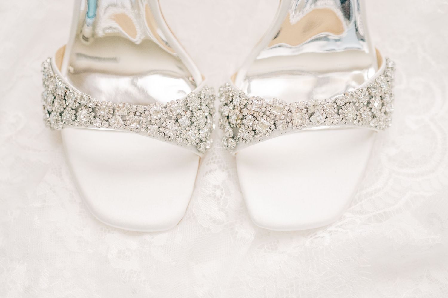 Elegant white bridal heels adorned with sparkling crystal embellishments resting on delicate lace fabric.