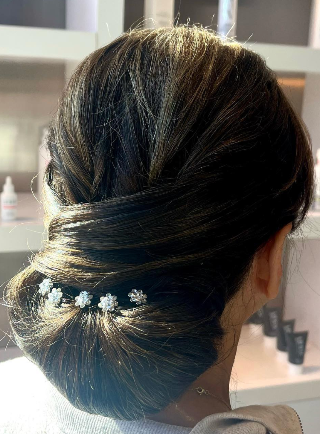 Elegant dark hair updo with delicate pearl flower pins, styled in a classic chignon at the nape of the neck.