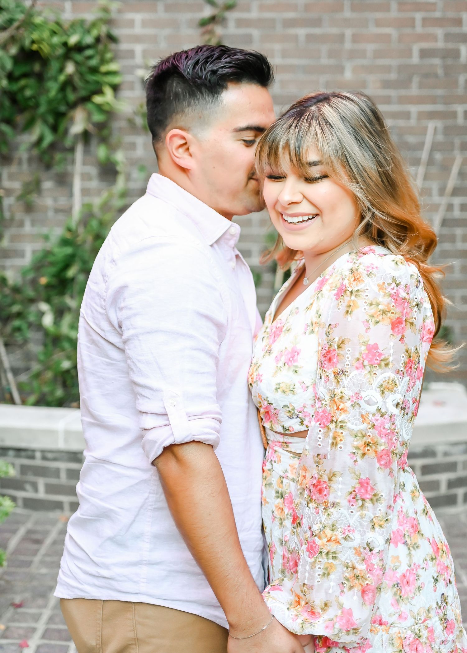 Man kissing smiling woman on the cheek while holding hands in a garden setting.