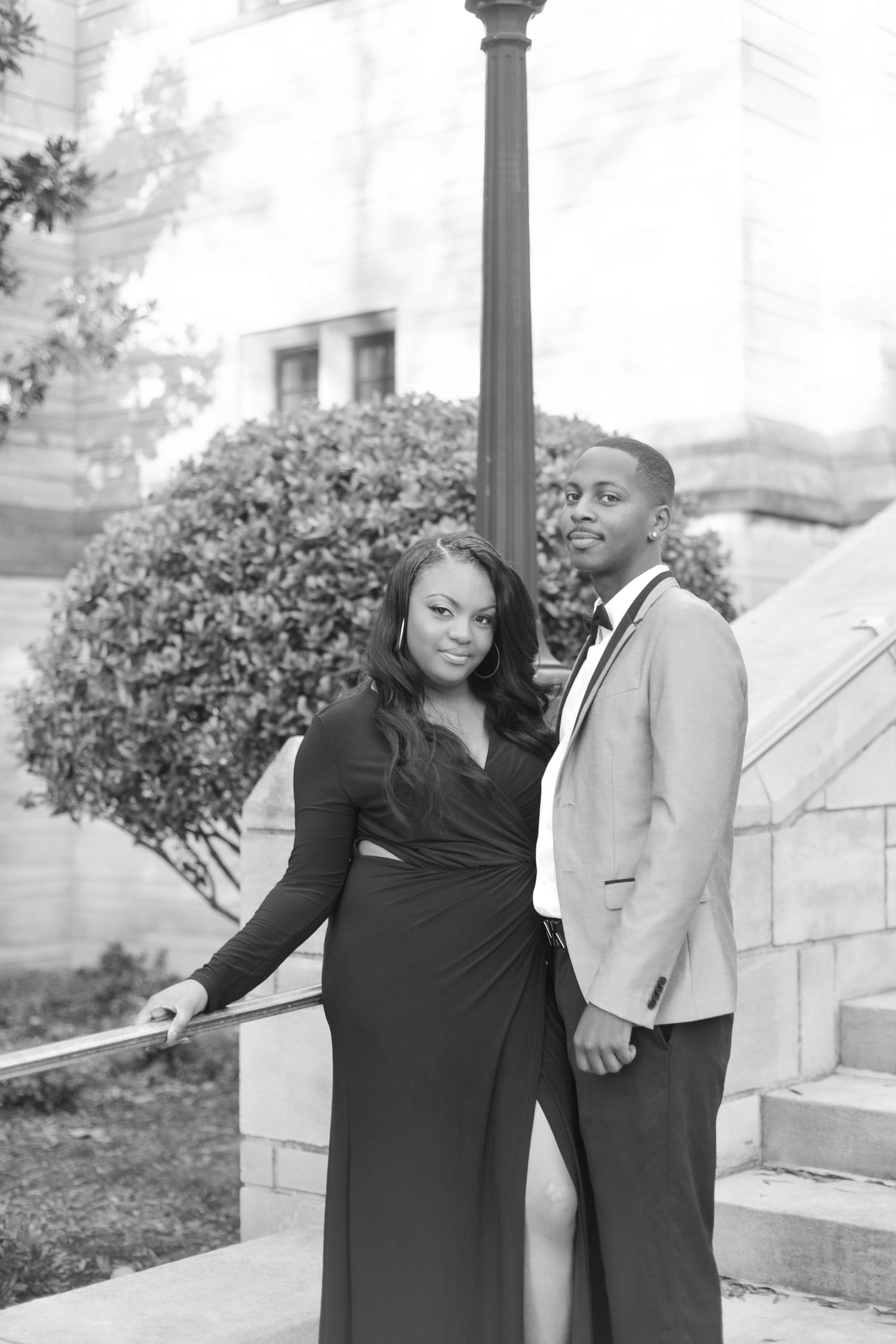 Black and white photo of an elegant couple posing outdoors, woman in black dress and man in suit jacket.