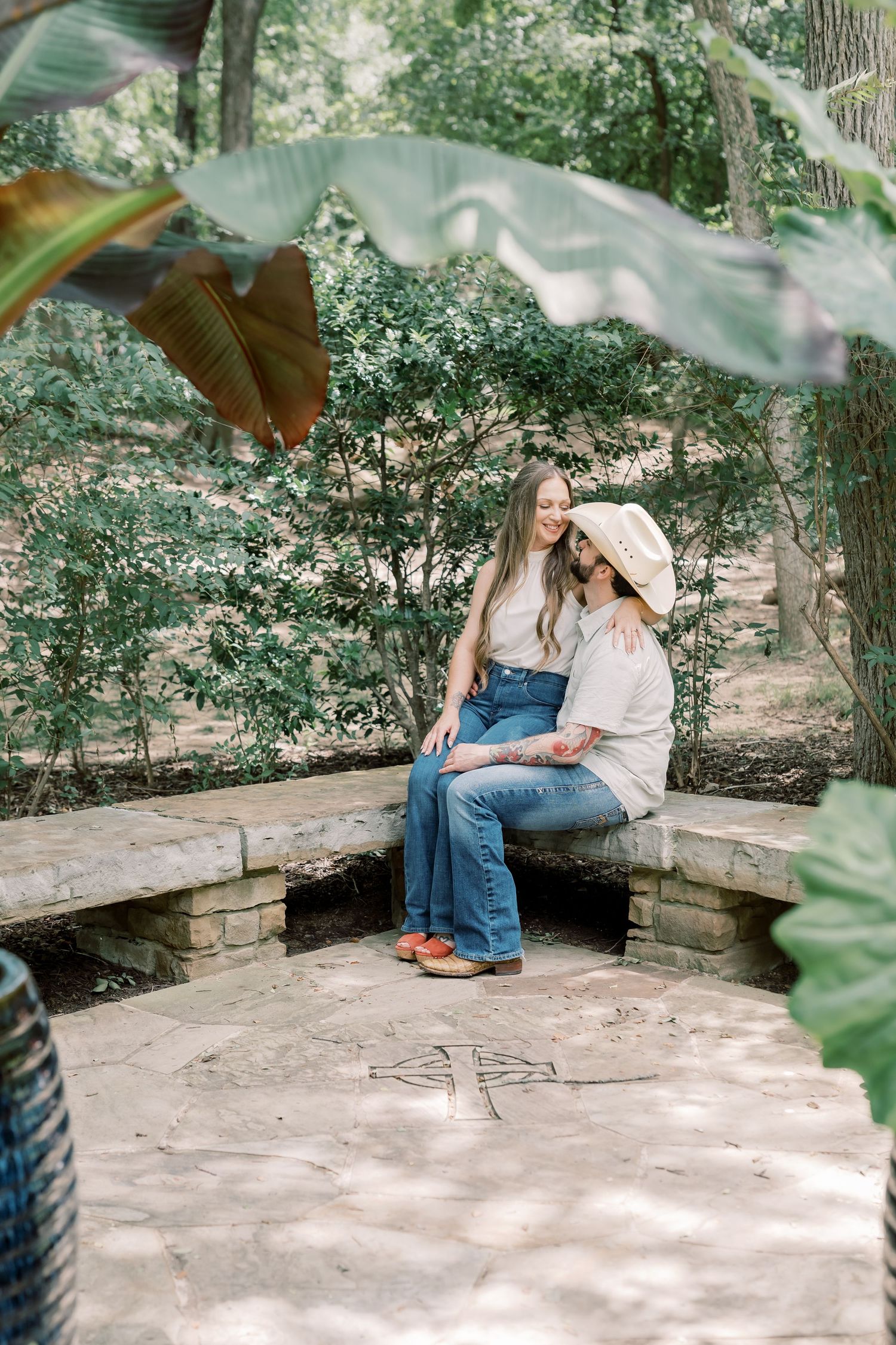 Couple sitting close together on a stone bench in a wooded garden.