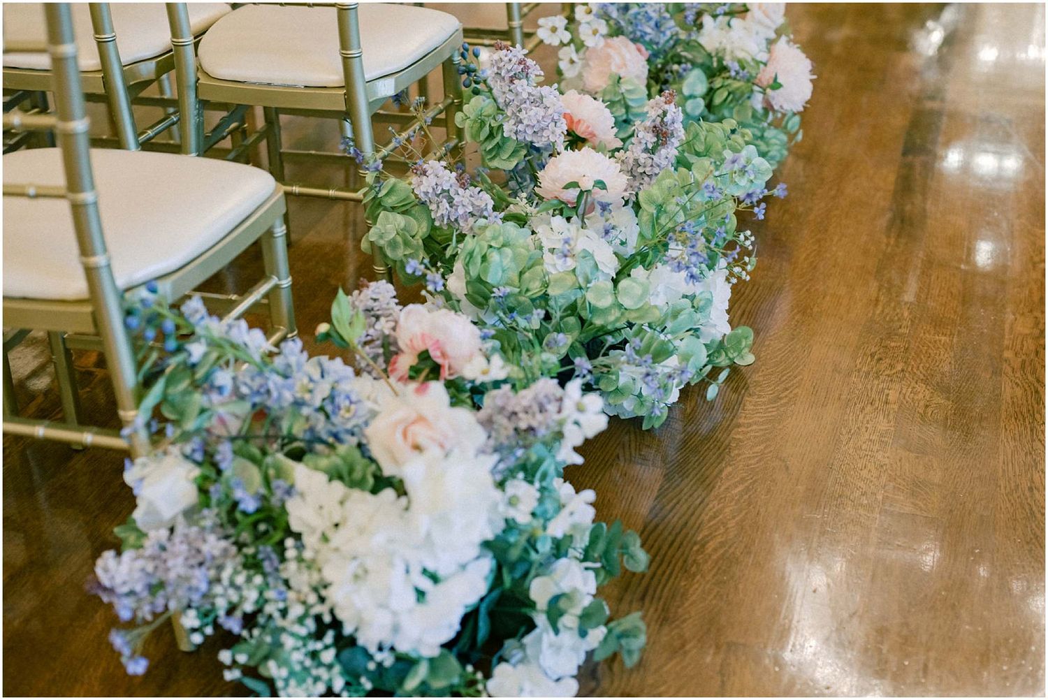 Wedding ceremony space decorated with pastel floral arrangements and white chairs.