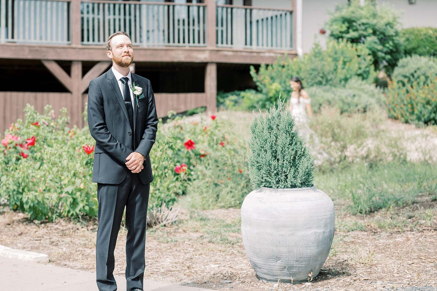 Groom in classic black tuxedo standing near decorative garden planters.