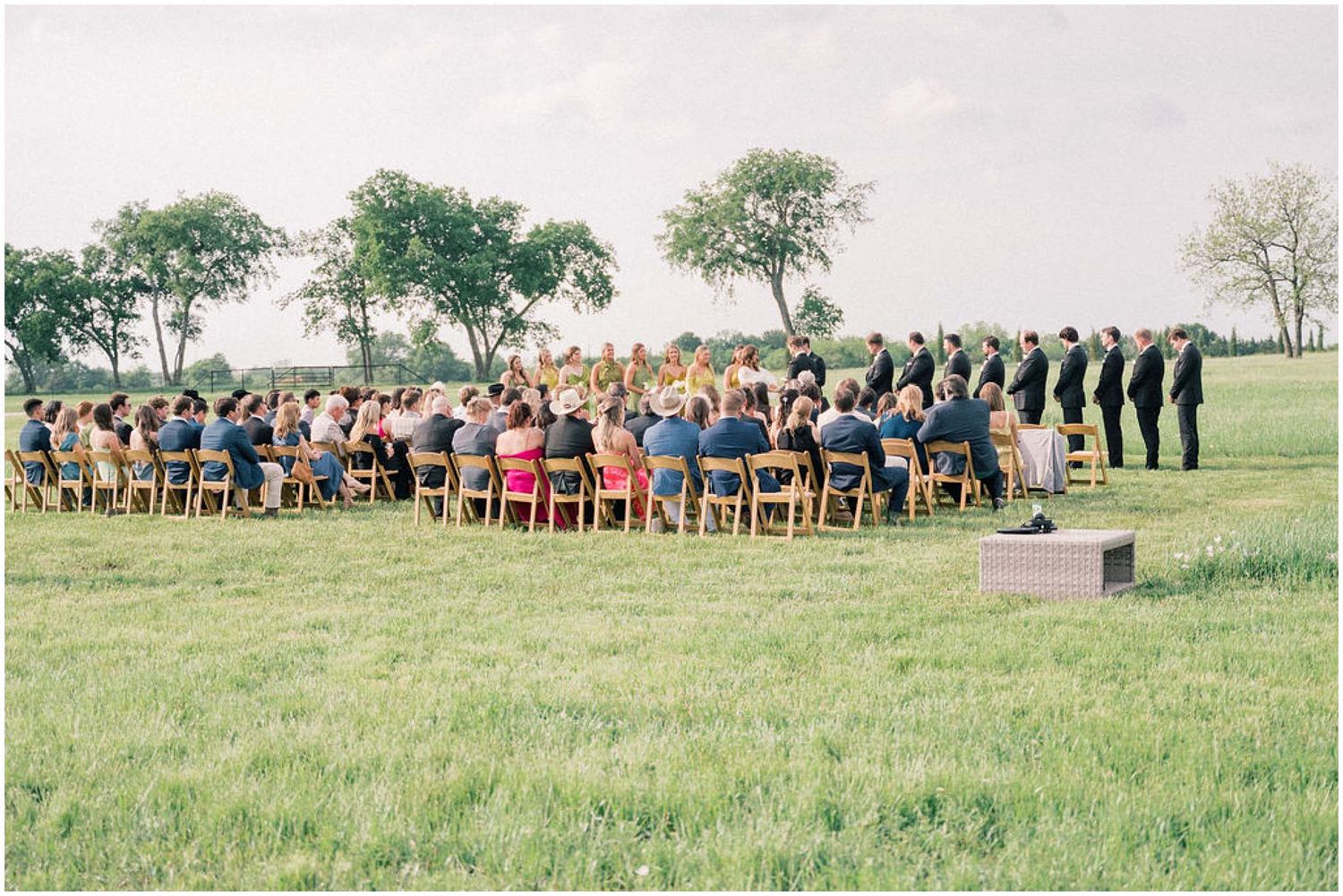 Wide angle view of wedding guests seated outdoors during daytime ceremony.