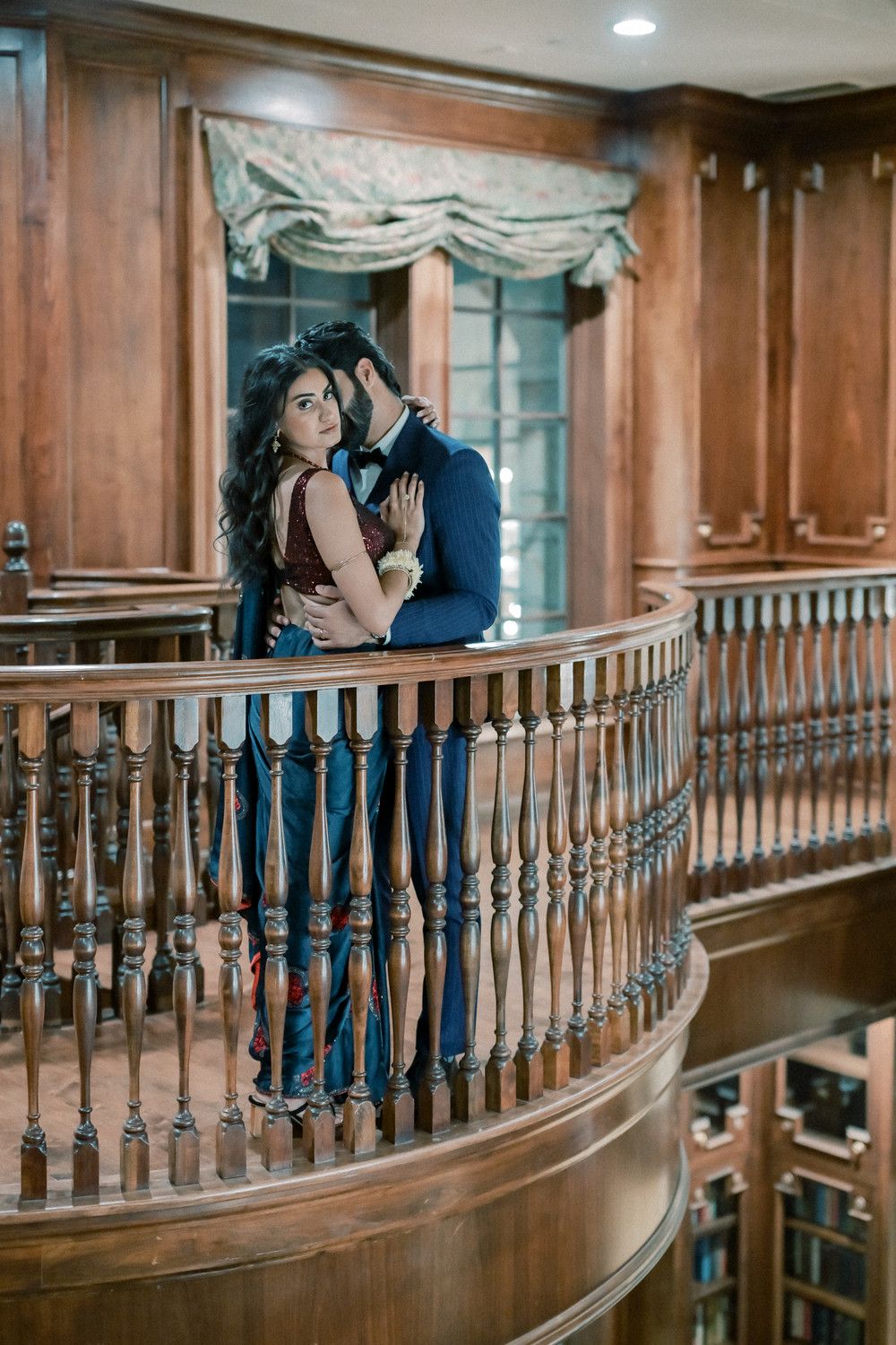 Couple shares intimate moment along curved wooden balcony with ornate railings.
