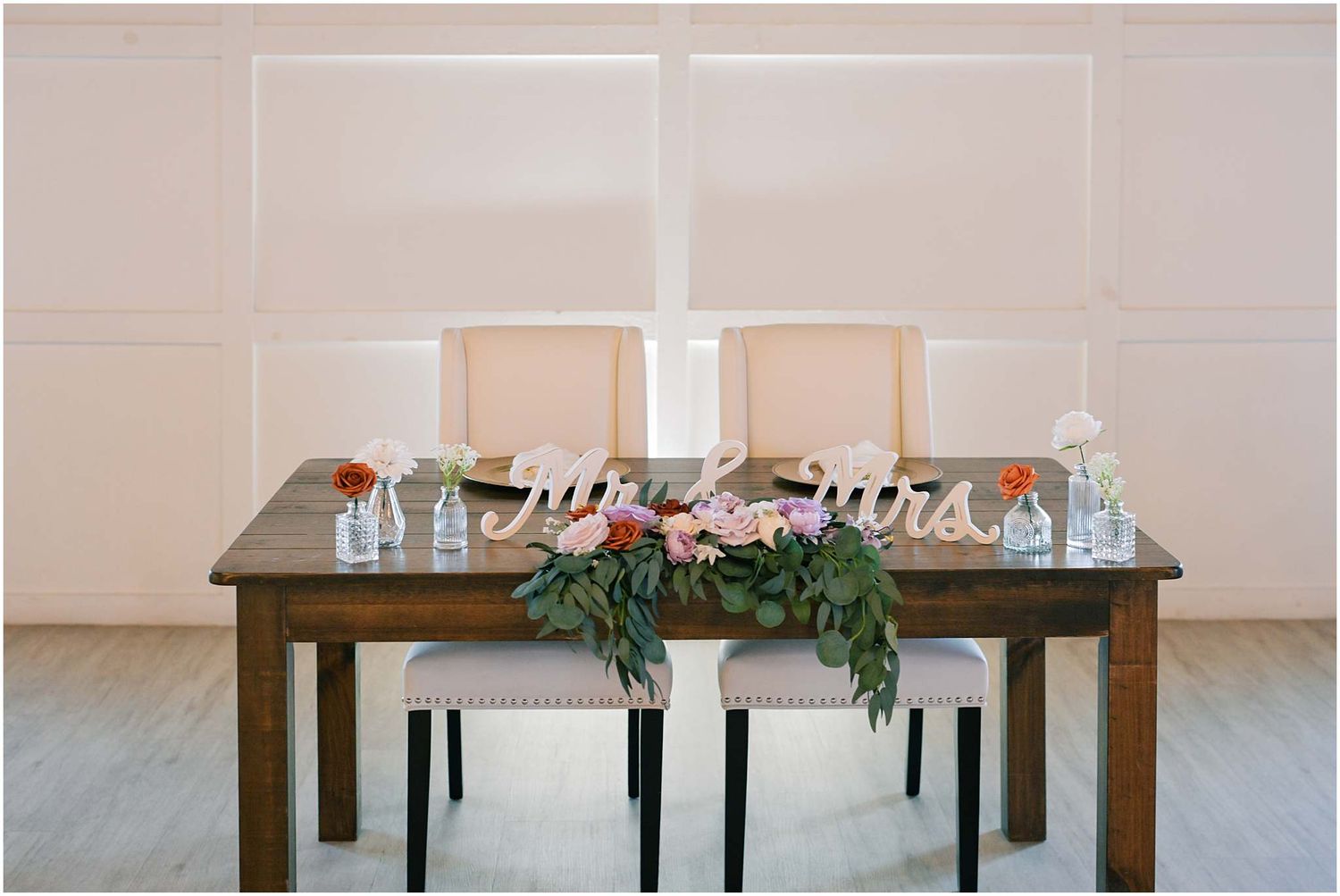Elegant wedding reception tables arranged with simple place settings and greenery accents.
