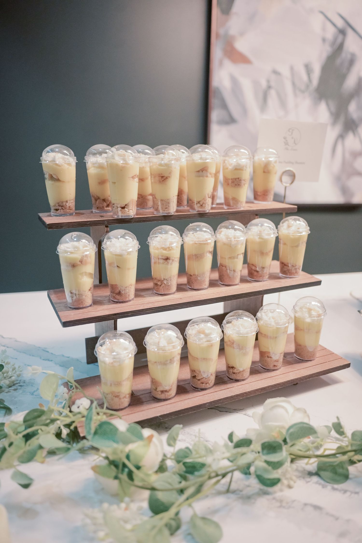 Three-tiered wooden display holds rows of layered dessert cups at an elegant wedding reception.