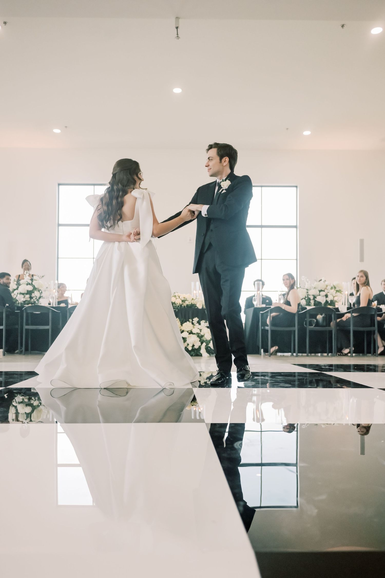 Bride and groom share their first dance on a black and white checkered floor in an elegant reception venue.