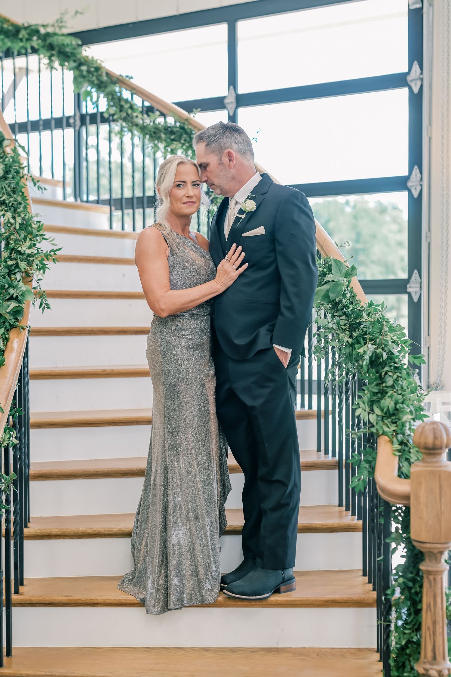 Elegant couple in formal attire posing on a staircase decorated with lush greenery garland.