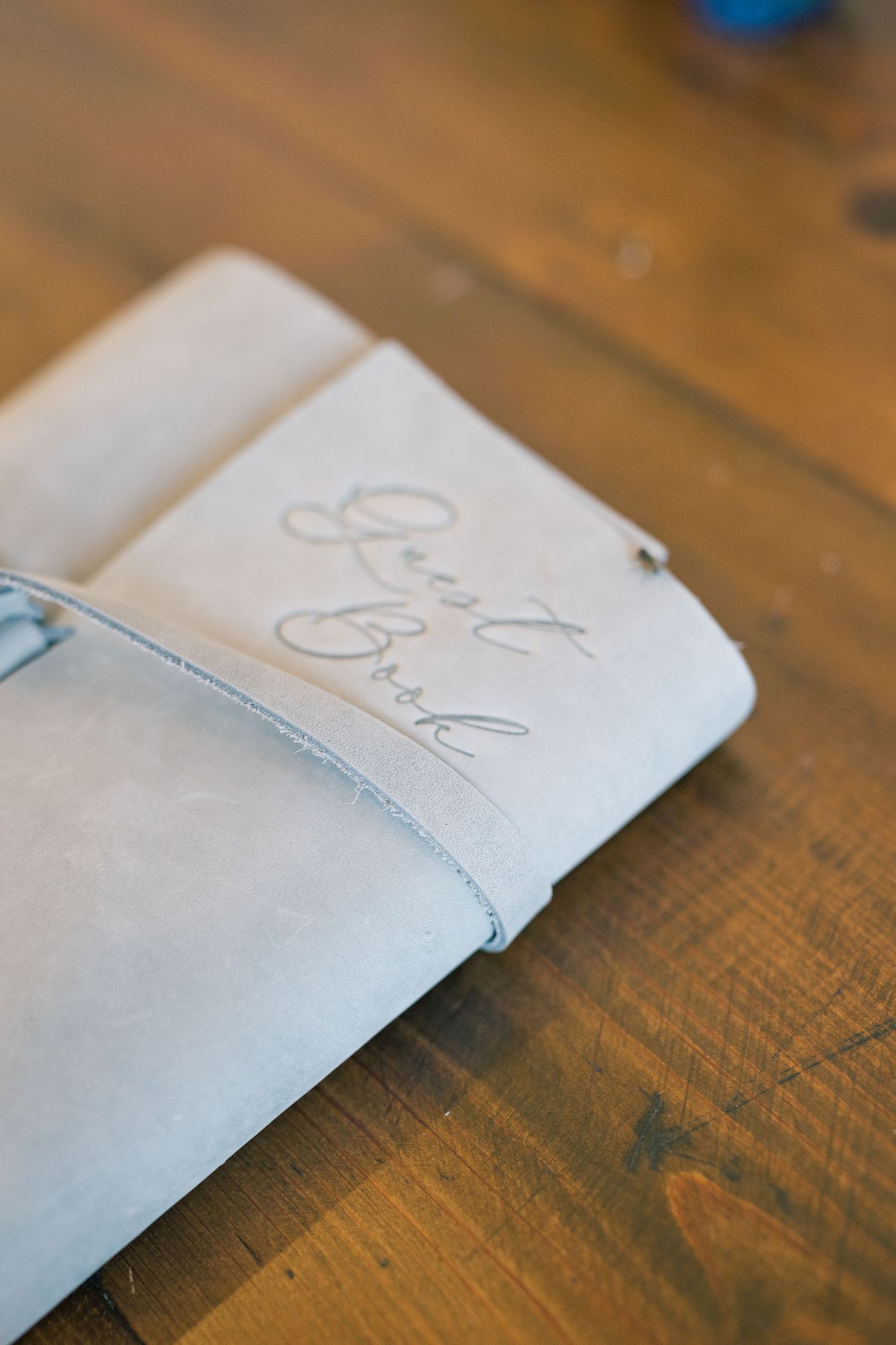 Elegant leather wedding guest book with embossed script lettering resting on a rustic wooden table.