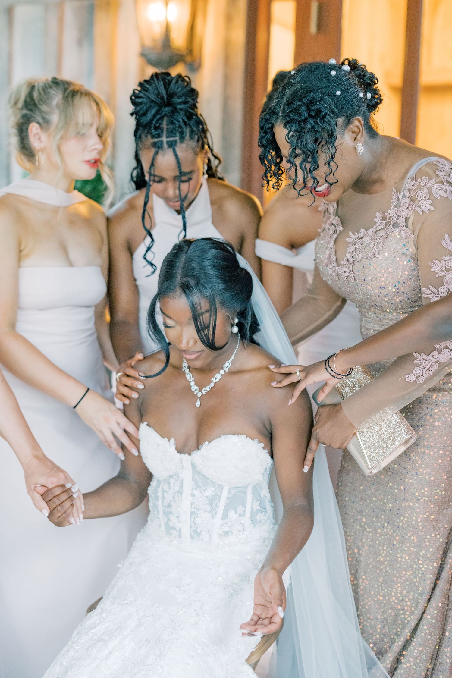 Bridesmaids and mother help Black bride in corset lace wedding gown with jewelry and veil.
