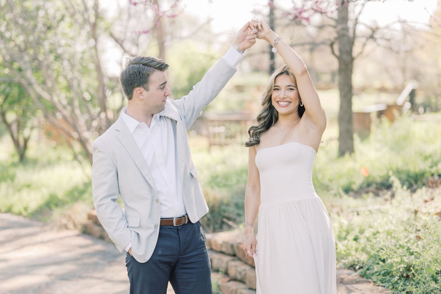 A couple in light colored formal attire poses together in a romantic outdoor garden setting during a photo session.