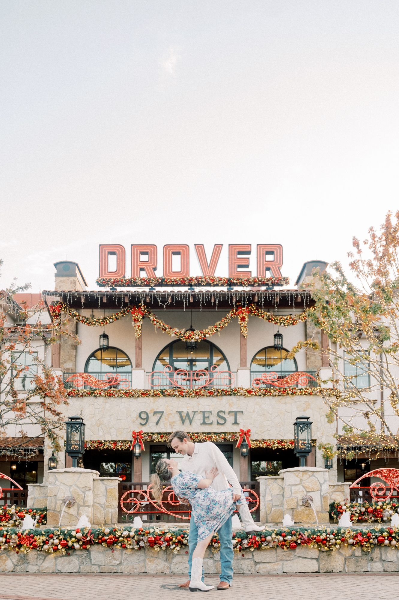 A couple poses in front of a vintage-style building with 'Draper' signage and festive holiday decorations.