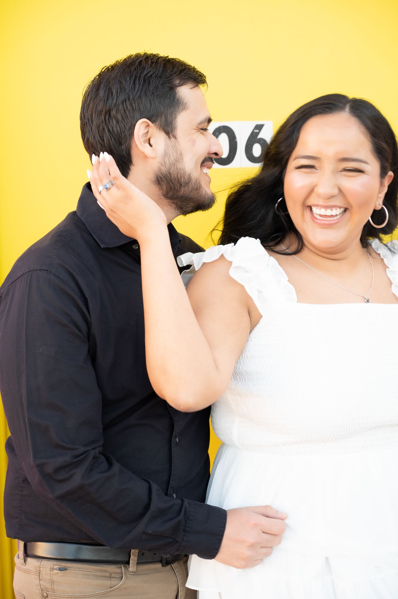 Happy couple in contrasting outfits sharing playful moment against yellow wall.