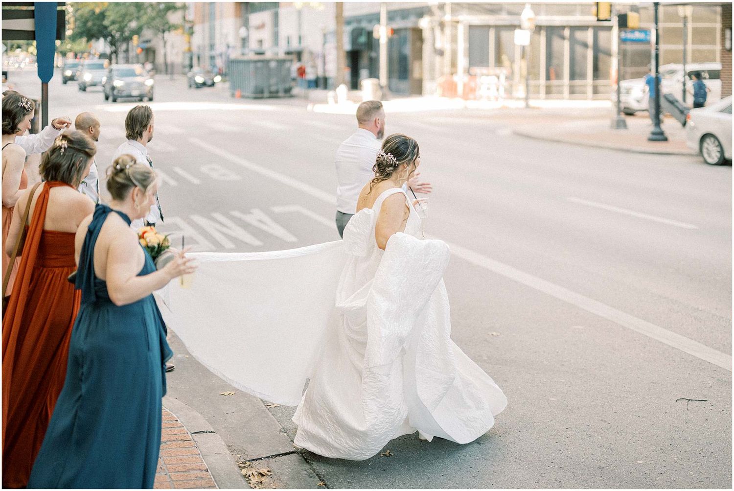Wedding party taking celebratory photos on a sunny urban street.