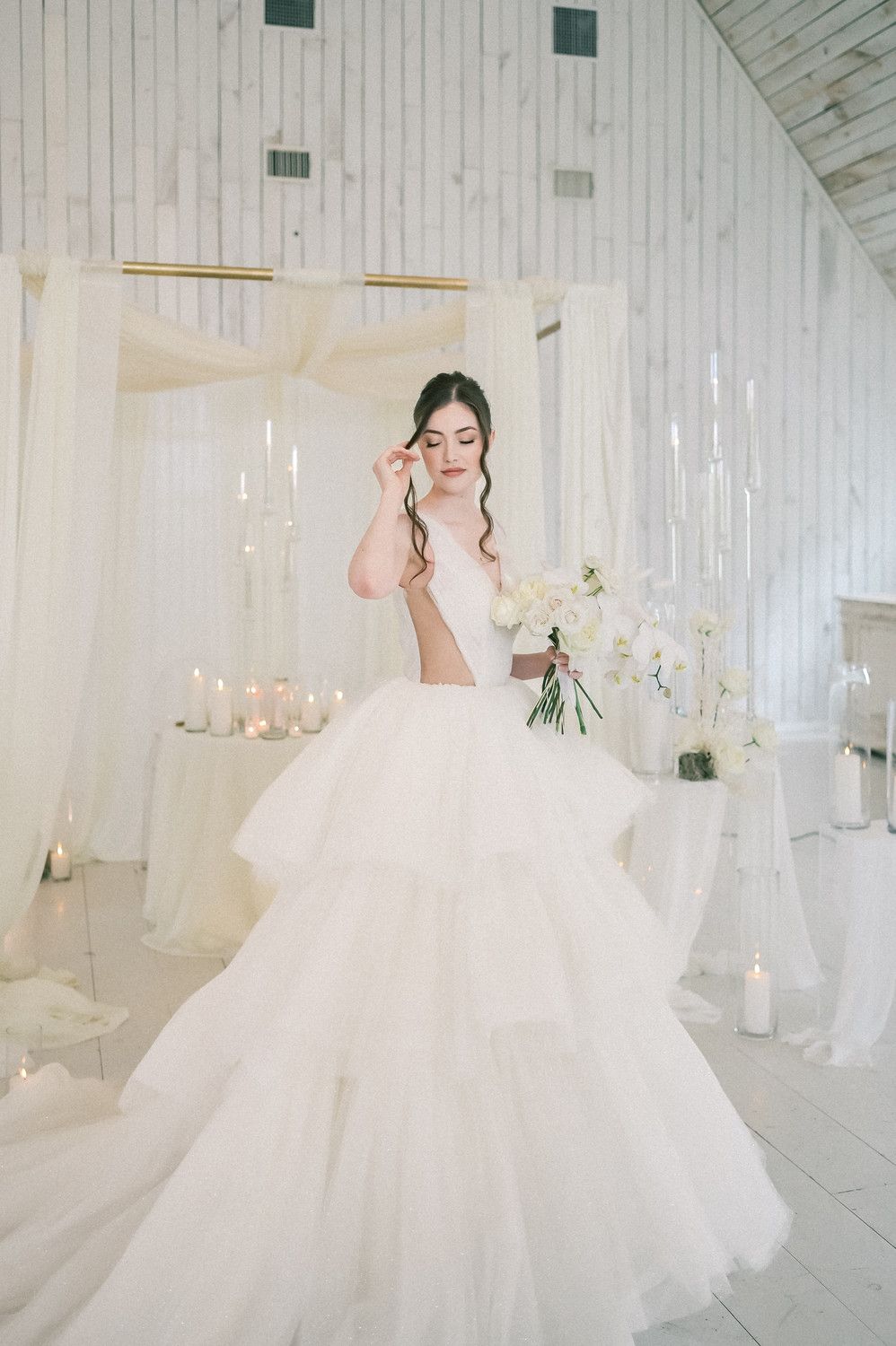 A bride in a voluminous white tulle ball gown poses in an elegant white room with crystal chandeliers.
