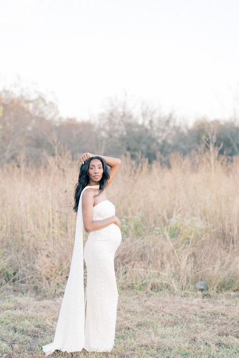 A maternity photoshoot in a serene field with tall grass during golden hour features a flowing white dress.